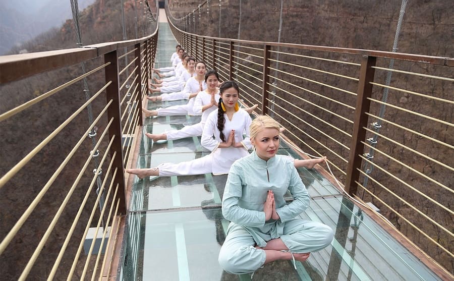 Women sitting along the glass bridge doing yoga 