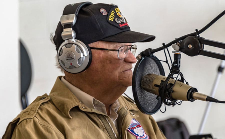 Norwood in uniform wearing headphones while sitting in front of a radio microphone 