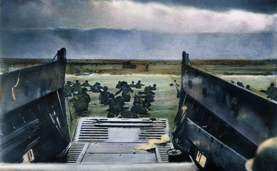 A landing craft with soldiers creeping through the water around it off of Omaha Beach during the invasion of Normandy 