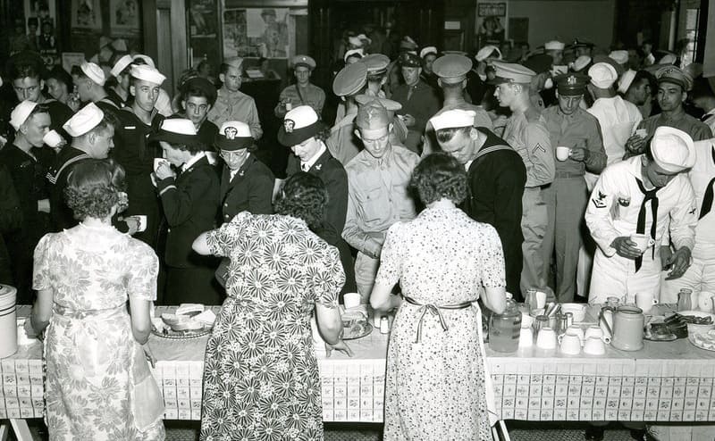 Woman in an assembly line handing out food to service members 