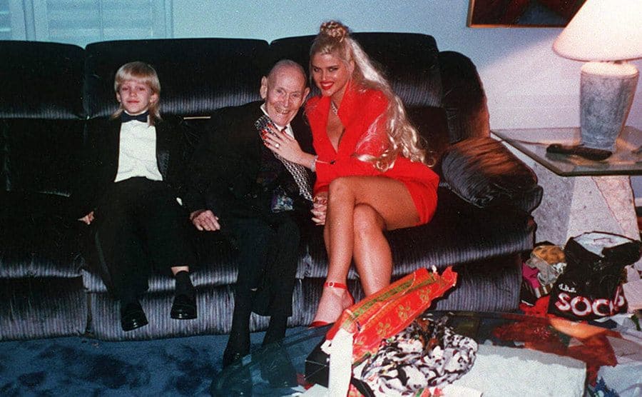 Anna Nicole and John Howard Marshall sitting on the couch together with a young boy near them 