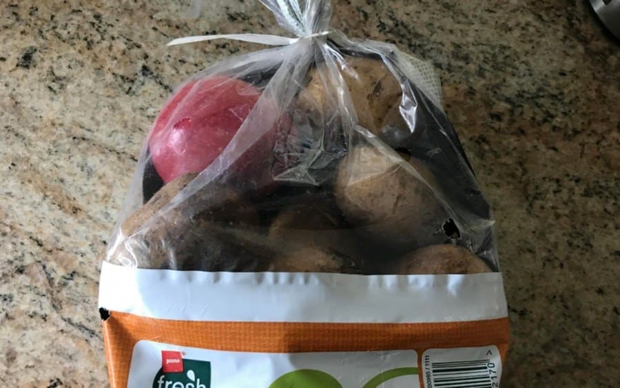 An apple inside a bag of potatoes