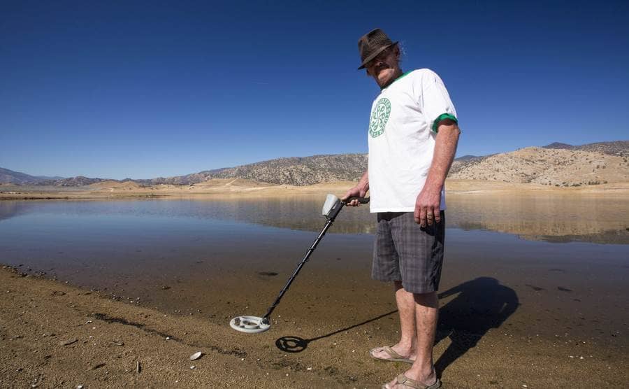 A man using his metal detector near a lake