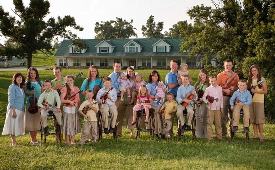 The entire Duggar family sitting outside with their instruments, a cute family portrait. 