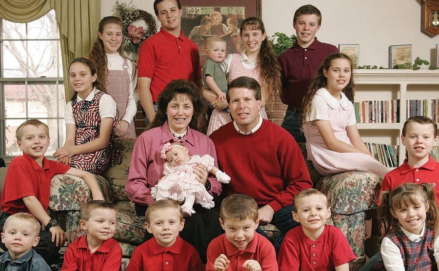 The Duggar family sitting for a portrait, all dressed in red clothing. 