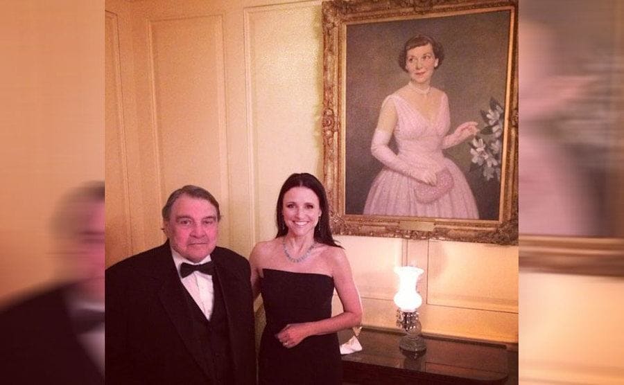 Julia Louis-Dreyfus posing with her father in front of an old painting of a woman 