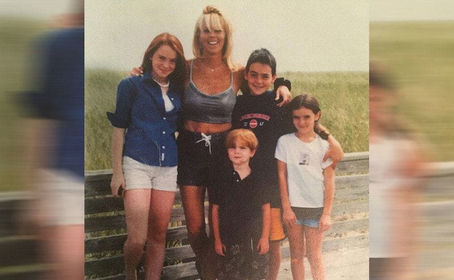 Lindsay Lohan with her mother and three siblings posing on the beach next to a grassy field 