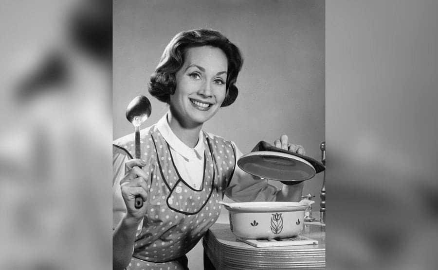 A smiling woman about to serve food out of a dish. 
