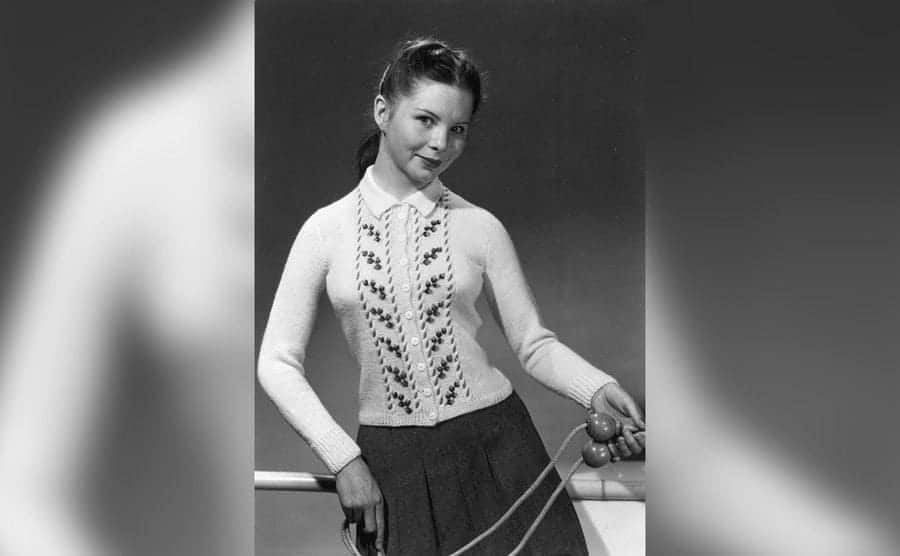 A coy schoolgirl is wearing a jumper and carrying a skipping rope.