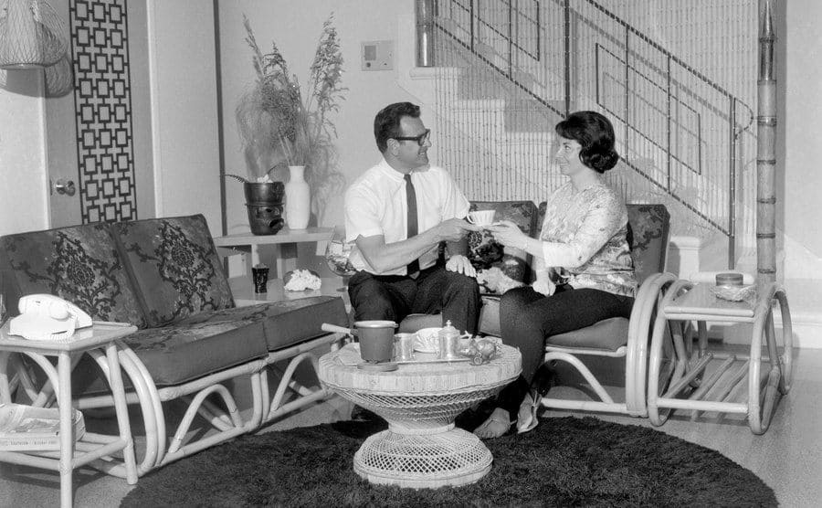 Man and woman share a cut of tea in a clean and organized living room. 