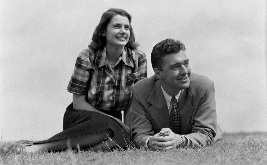 A young couple sitting on the grass white looking off into the distance. 