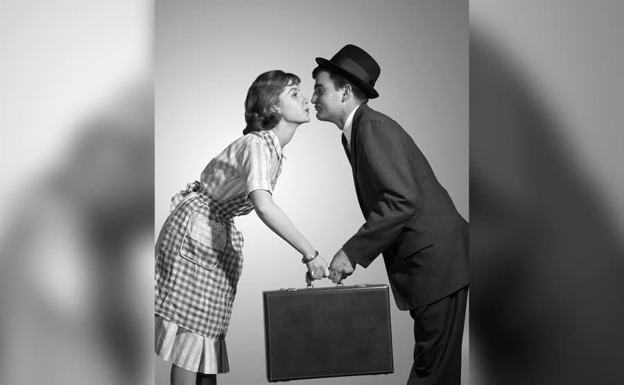 A housemaker wife is leaning into kiss Businessman as she hands him briefcase. 