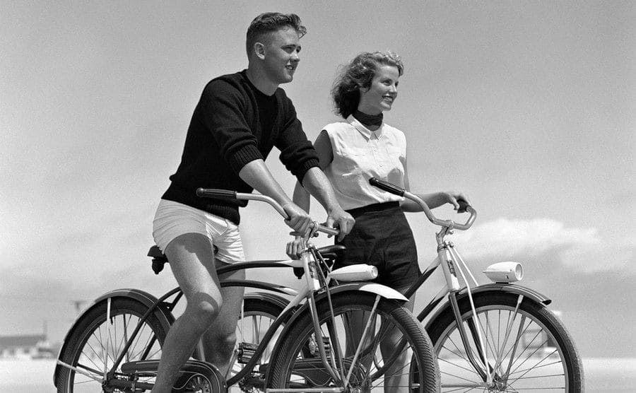  Teenage boy and girl ride bikes on the beach as part of their date. 