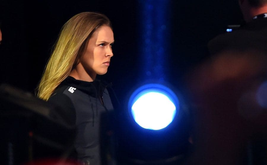 Ronda Rousey looking intensely forward with a spotlight to her left 
