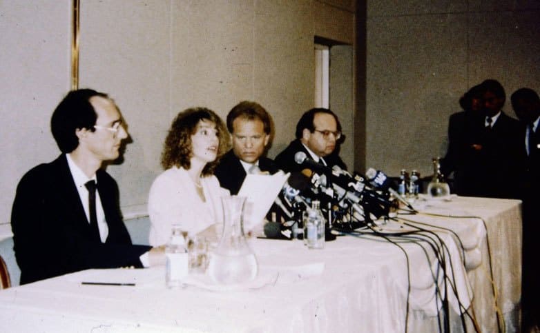 Dr. Jerome Oziel with his wife and others sitting at a press conference desk 