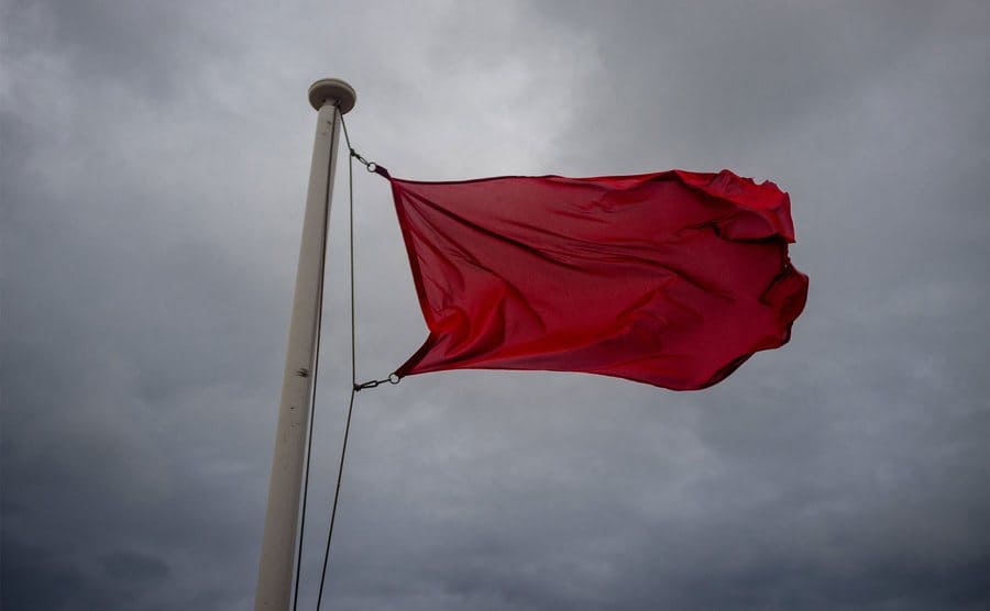 Red flag-waving to indicate wind hazard alert on the beach.