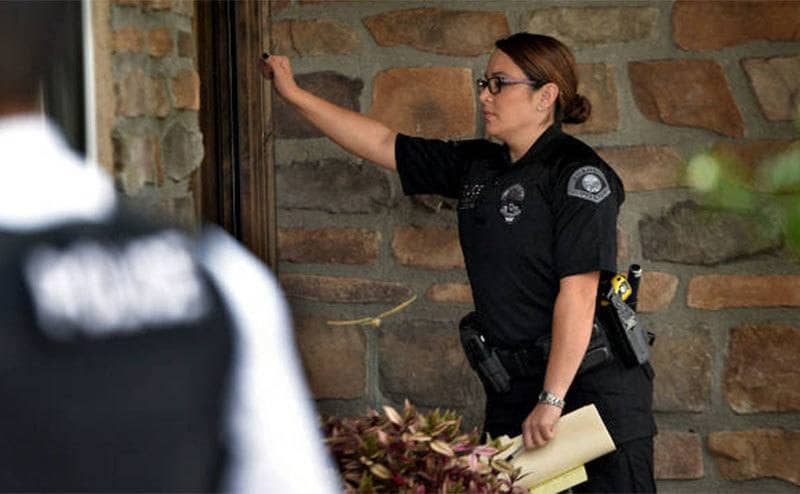A female police officer is knocking on the front door of a home. 