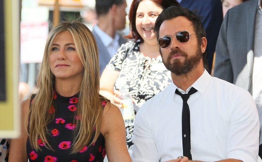 Jennifer Aniston and Justin Theroux holding hands sitting in a crowd 