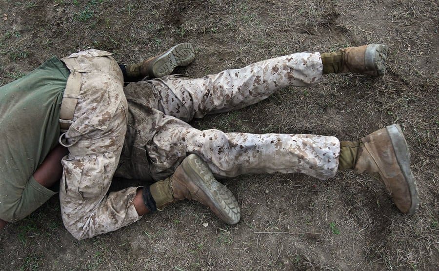 A cropped view of a marine holding down another one while sitting on his back. 