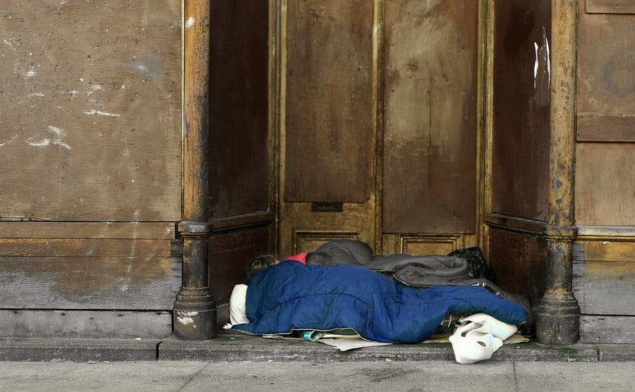 A homeless person is sleeping at the entrance of an abandoned building.