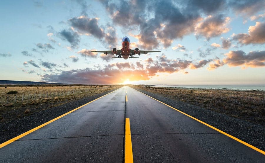 An airplane is flying over a highway road at sunset.