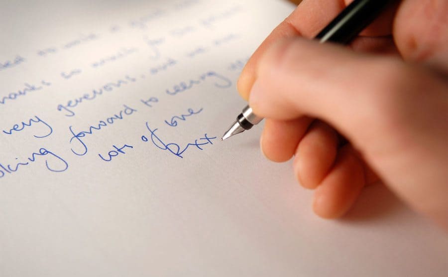A hand holding a fountain pen and writing a letter. 