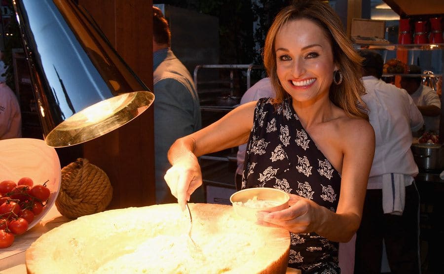 Giana serving vegetables out of a large wheel of parmesan cheese.