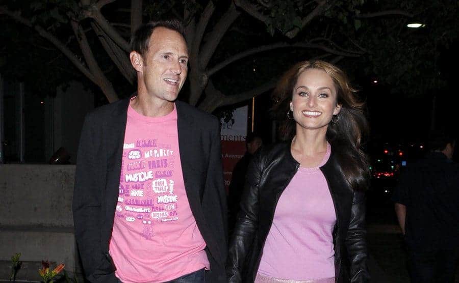 Todd Thompson and Giada walking down the street, both wearing pink shirts and a black jacket over 