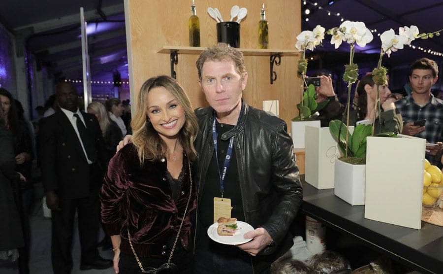 Giada with Bobby Flay holding a plate with a sandwich at an event 