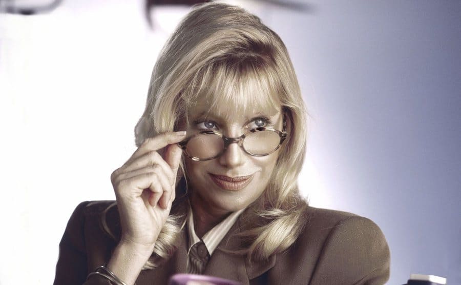 Suzanne Somers holding her glasses towards the tip of her nose 
