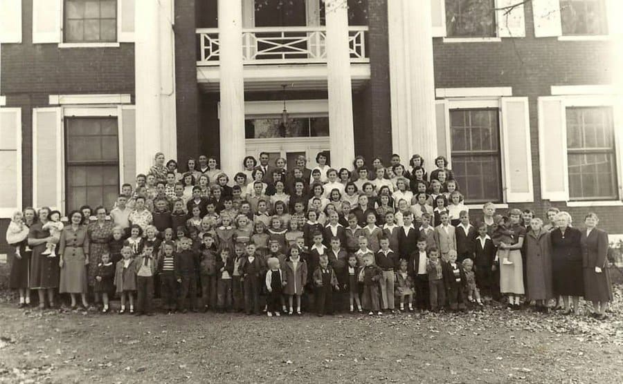 Children up for adoption and social workers posing for a group photo outside of a home. 
