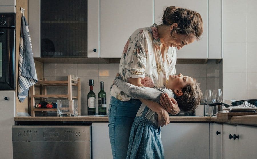 Mother and daughter in a loving embrace while standing in the kitchen. 