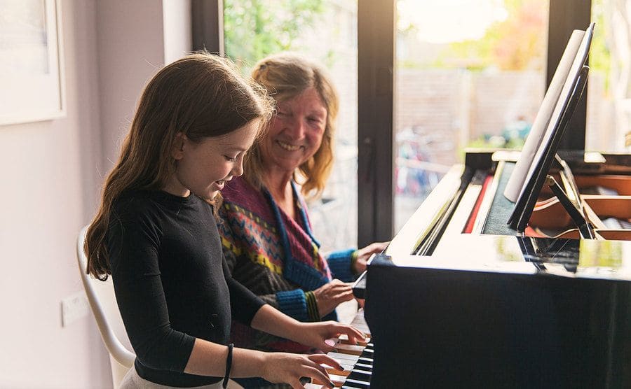 Young girl playing the piano with her teacher. 