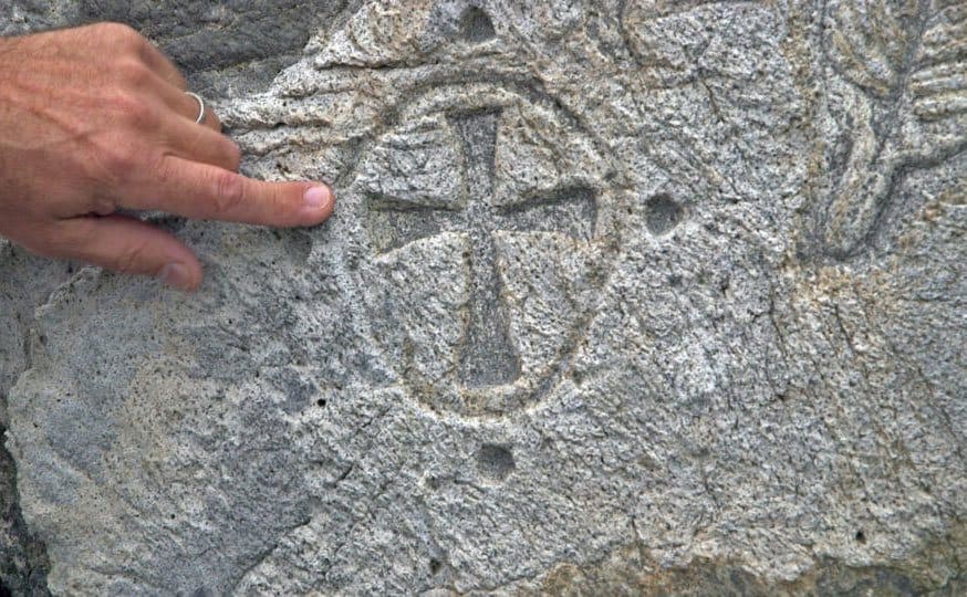 A finger pointing at a carving of a cross made in the stone. 