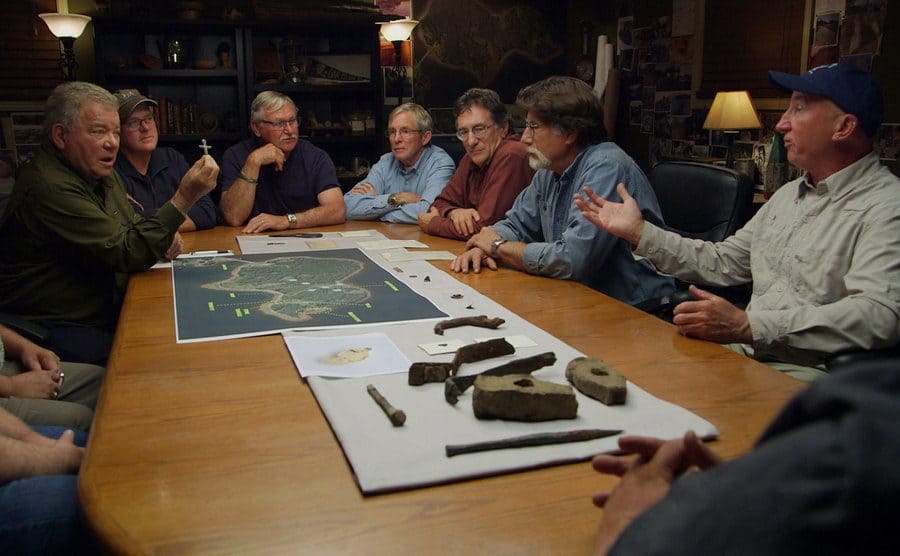 The crew on Oak Island is sitting around the table discussing the artifacts they have found. 
