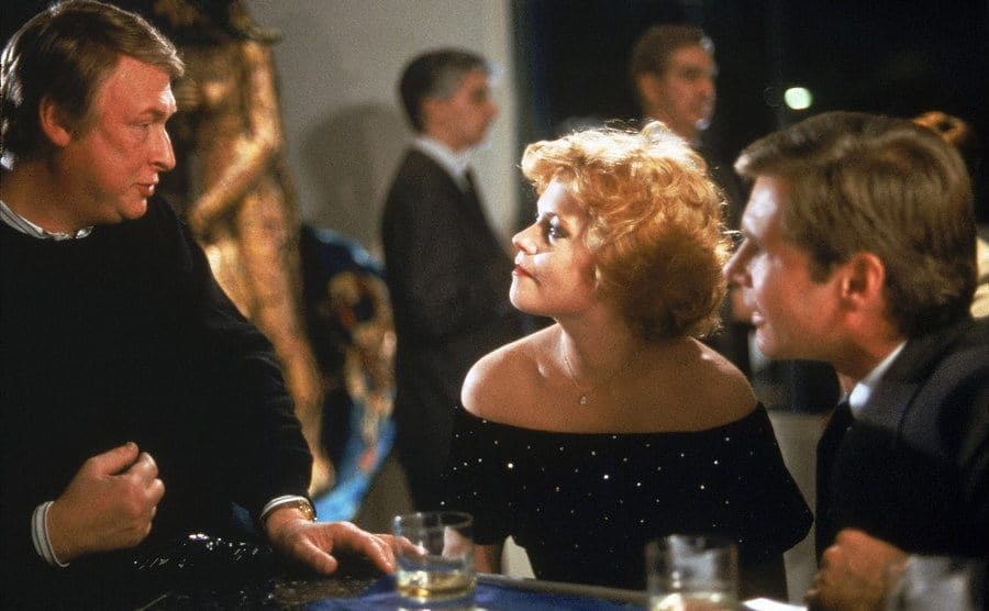 Mike Nichols speaking to Melanie Griffith and Harrison Ford at a bar 