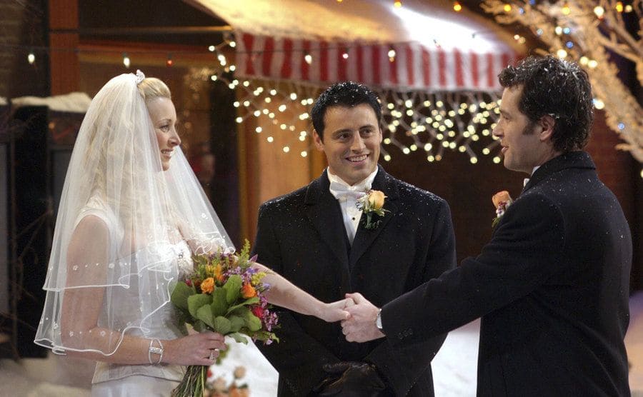 Lisa Kudrow y Paul Rudd tomados de la mano frente a frente en el día de su boda con Matt LeBlanc iniciando la ceremonia 