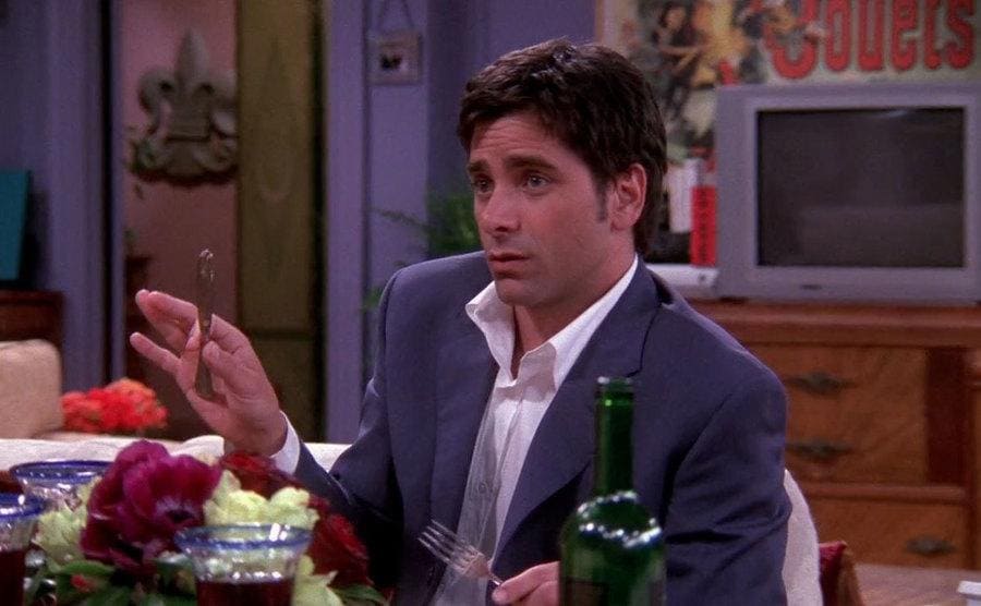 John Stamos luciendo un poco incómodo mientras cena en el apartamento de Mónica y Chandler 