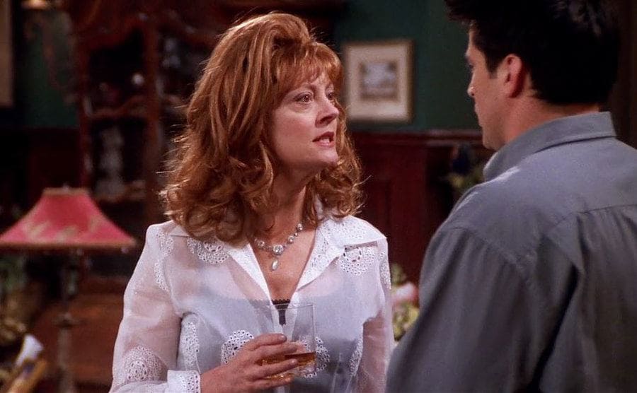Susan Sarandon con una copa en la mano hablando con Matt LeBlanc en una escena de Friends