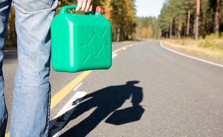 A man is standing on a countryside road with a petrol can. 