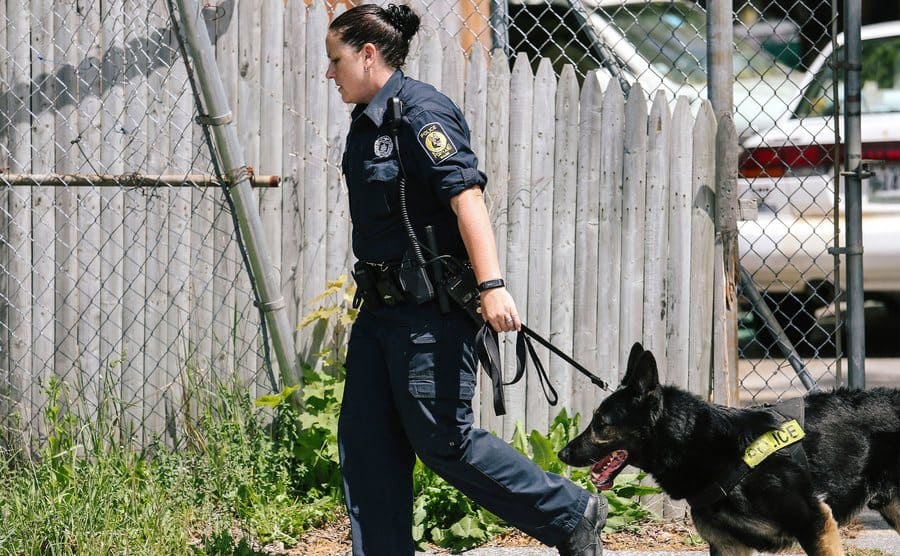 K-9-unit officer leads a police dog outside a home. 