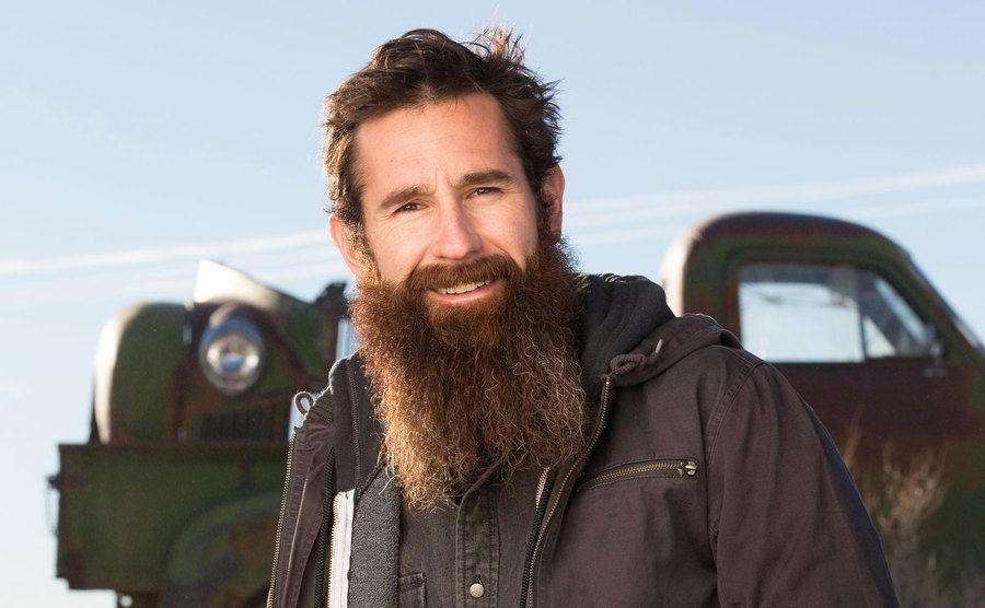 Aaron Kaufman is leaning on the hood of an old car. 