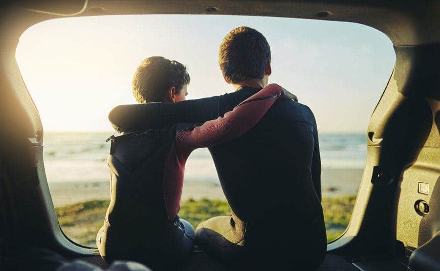 Rearview shot of two unidentifiable brothers sitting in the back of a car at the beach embracing one another. 