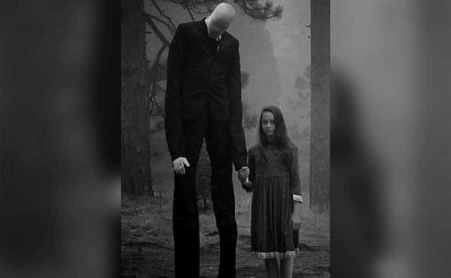 A little girl is holding the hand of the Slender Man in the woods. 