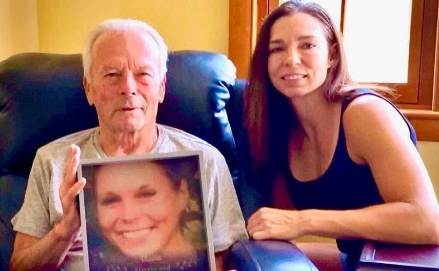 Julie Murray sits down with her father, Fred Murray, holding up a photo of Maura. 