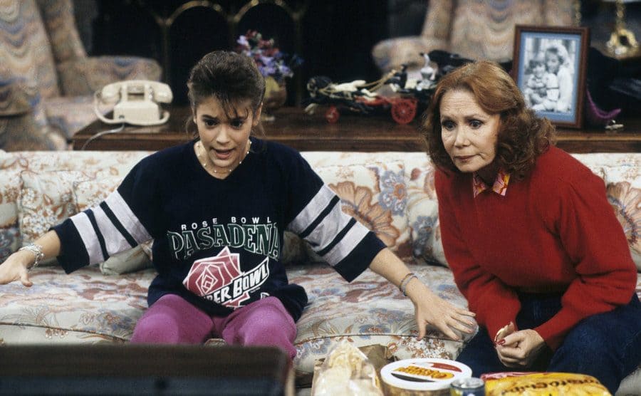 Alyssa Milano and Kathrine Helmond are watching tv on the couch in a scene from “Who’s the Boss?”. 