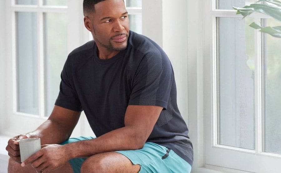 Michael Strahan is sitting next to a window frame.