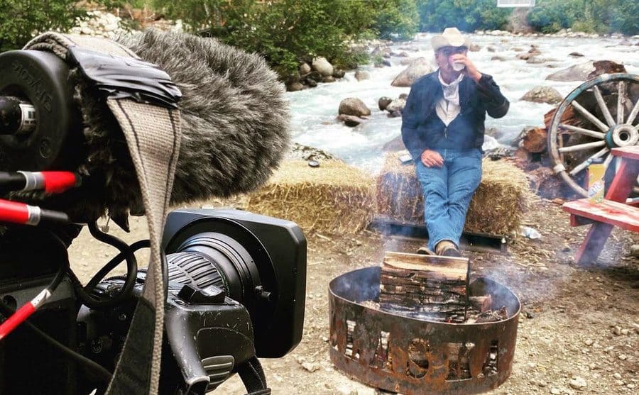 Marty Raney is being filmed as he sits and drinks coffee behind a campfire.