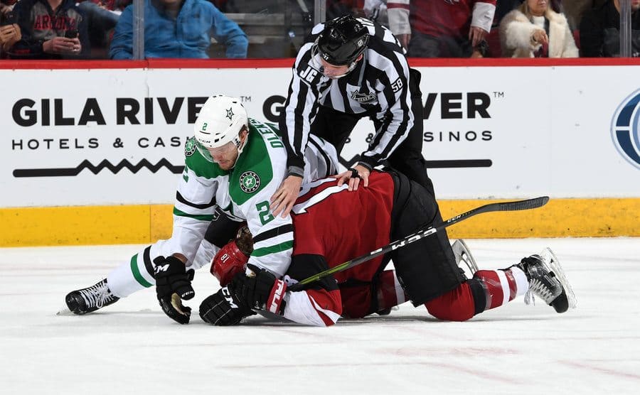 A referee attempts to separate two hockey players who are fighting on the ice. 