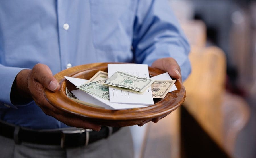 A man holds an offering plate in church. 